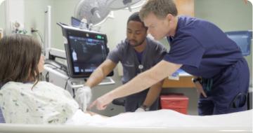 A photo of a resident and a provider training at the bedside of a patient.